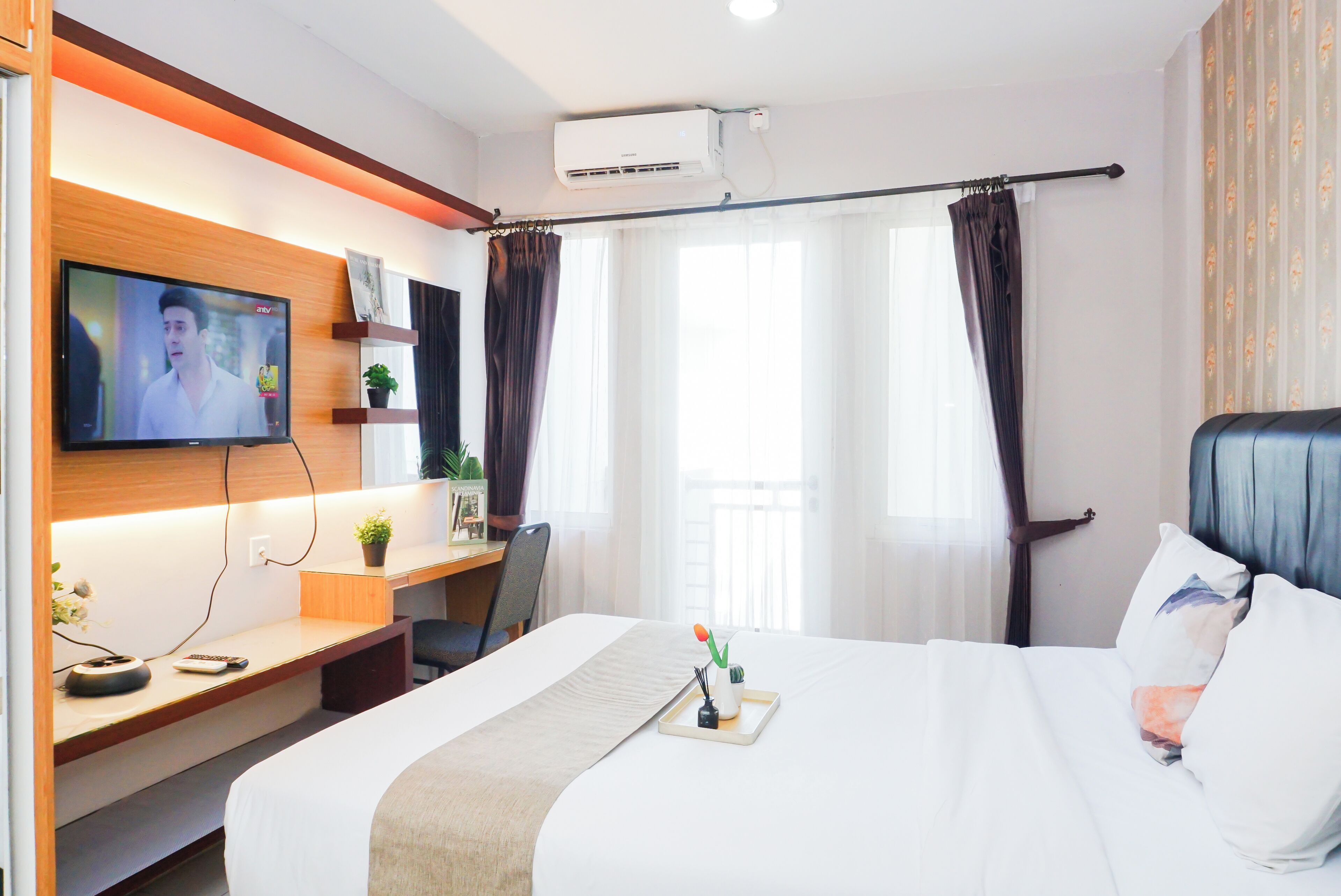 Habitación de hotel con cama, escritorio con televisor, planta y ventana con cortinas.