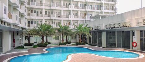 A modern apartment building with a central swimming pool surrounded by palm trees and a wooden deck.