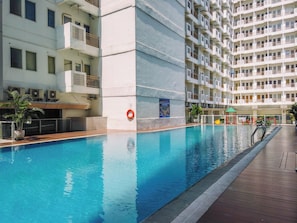 Piscina com deck de madeira, rodeada por edifícios residenciais com varandas.