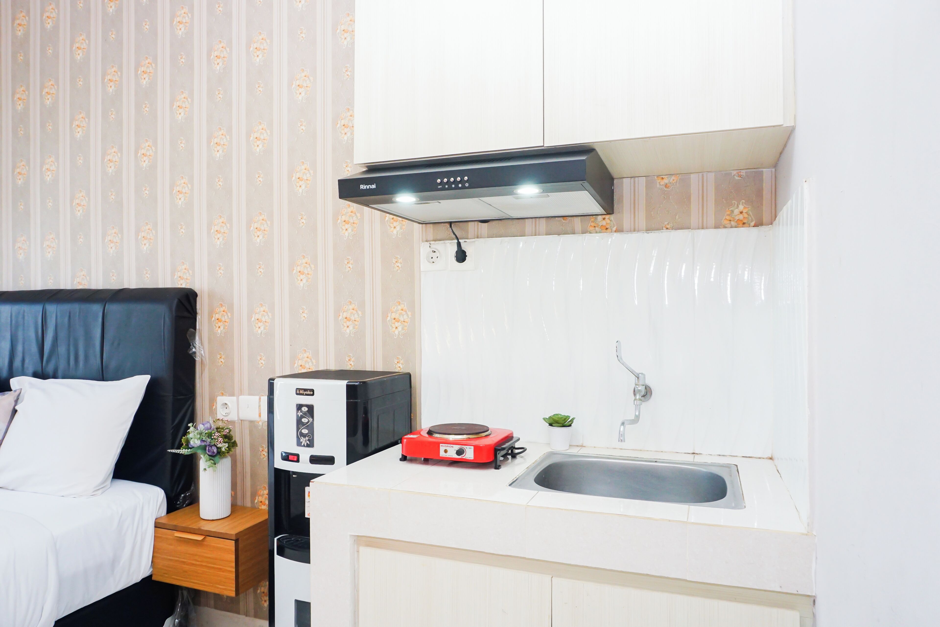 Una kitchenette compacta con microondas, placa de inducción roja, lavamanos y un armario.