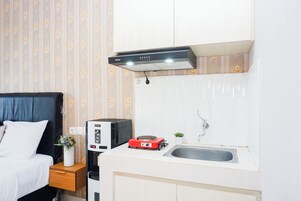 Una kitchenette compacta con microondas, placa de inducción roja, lavamanos y un armario.