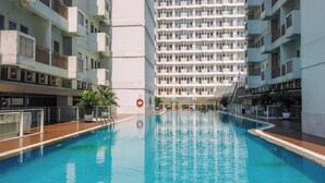 A swimming pool surrounded by a multi-story building with balconies and air conditioning units. - Comfortable Living Studio At Apartment Sentul Tower (Bogor)