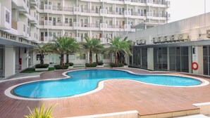 A modern apartment building with a central swimming pool surrounded by palm trees and a wooden deck. - Comfortable Living Studio At Apartment Sentul Tower (Bogor)