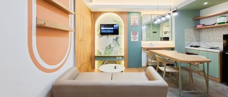Una habitación de hotel moderna con sofá, una mesita, televisor y kitchenette.