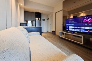 A modern living room with a flat-screen TV, a sofa, a kitchen area, and a wooden floor.