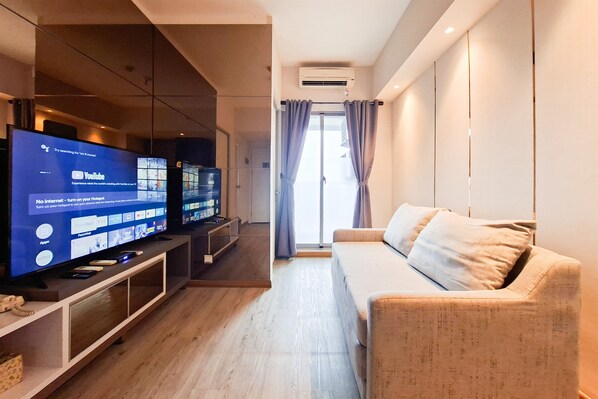 A modern living room with a flat-screen TV, a sofa, and a wooden floor.