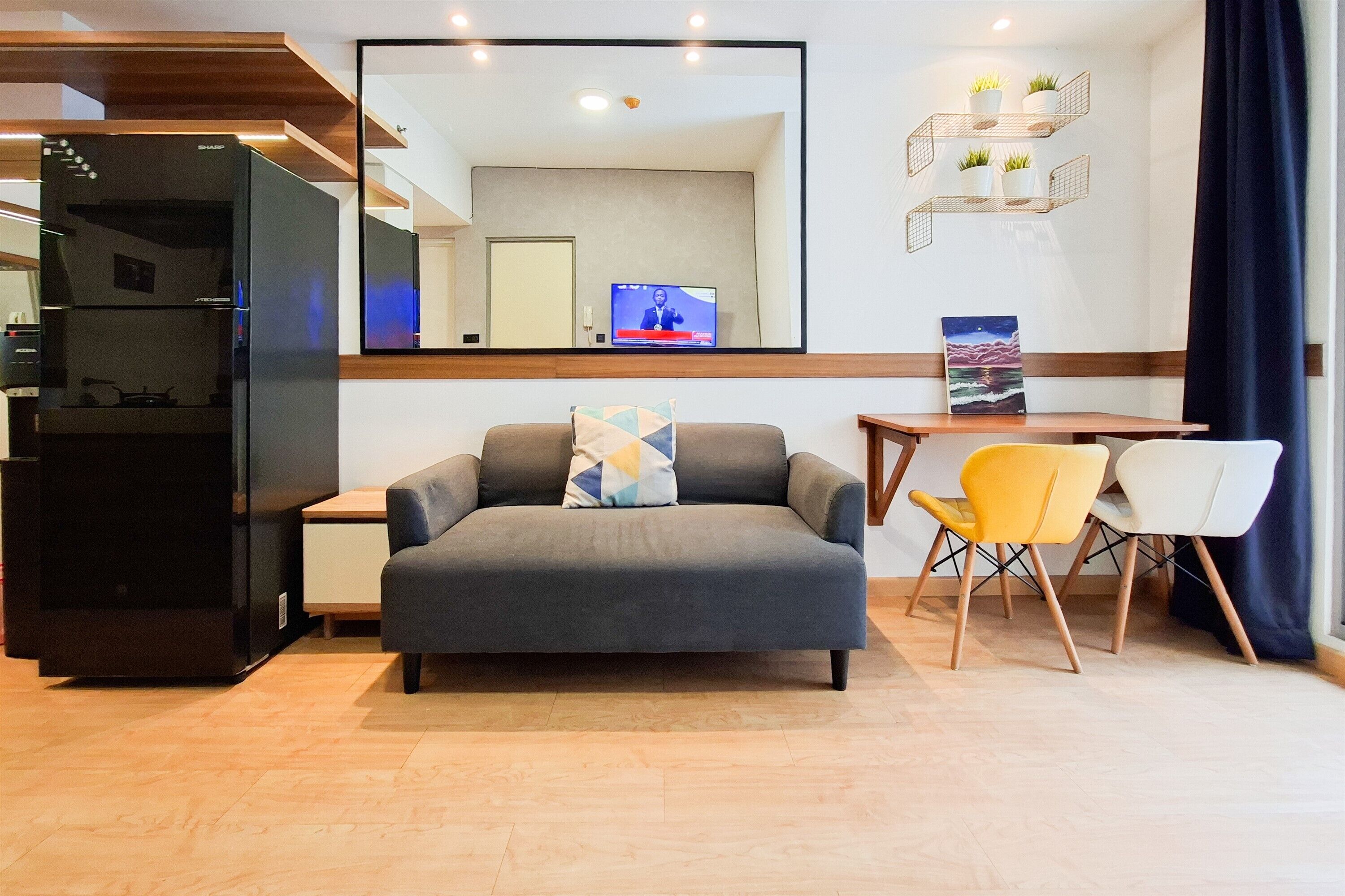 Ein modernes Wohnzimmer mit einer Couch, einem Esstisch mit Stühlen, einem flachbildfernseher an der Wand und einer Küchenzeile inklusive Kühlschrank.