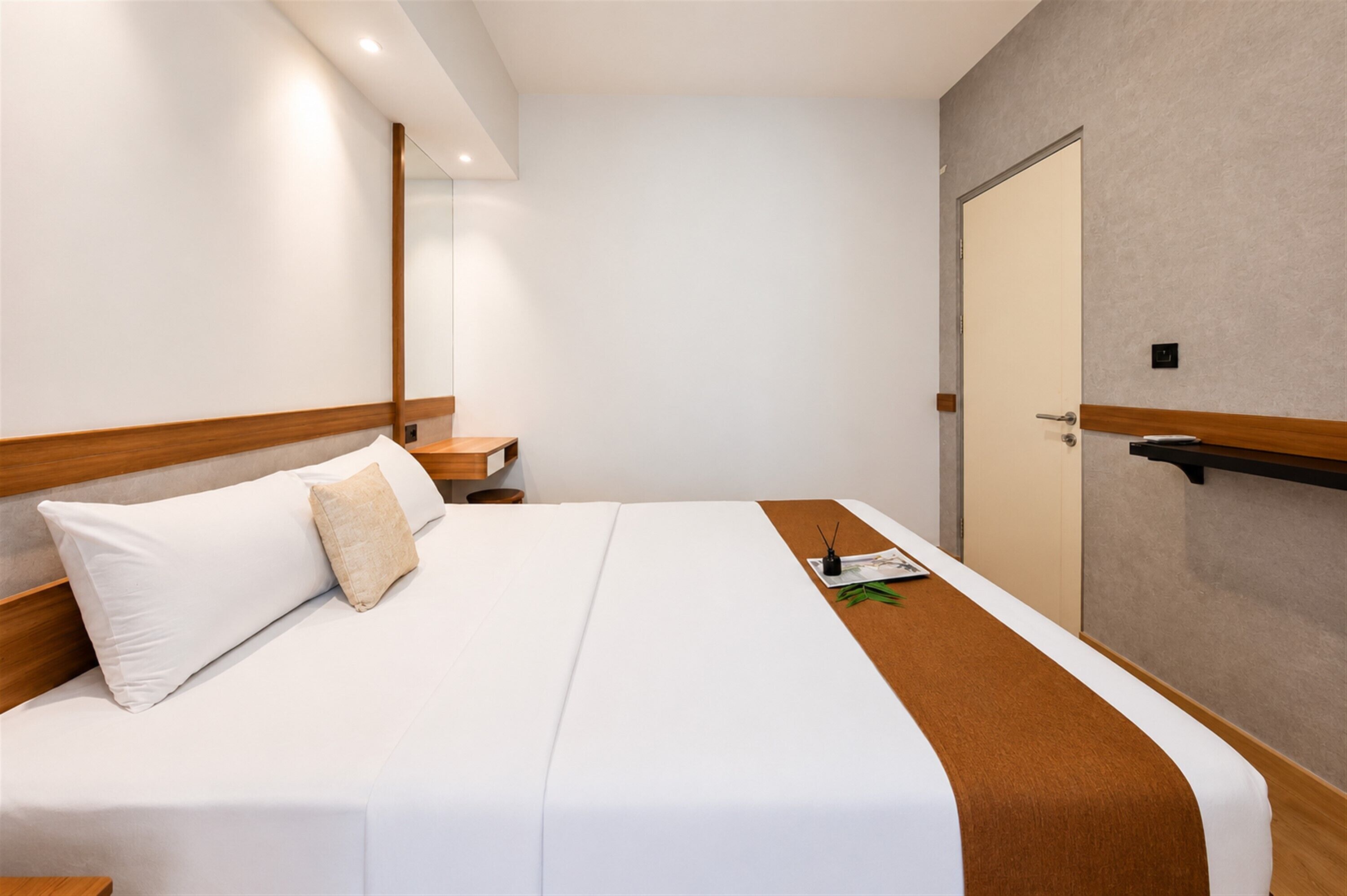 A hotel room with a bed, a bedside table, a nightstand, a mirror, and a door.