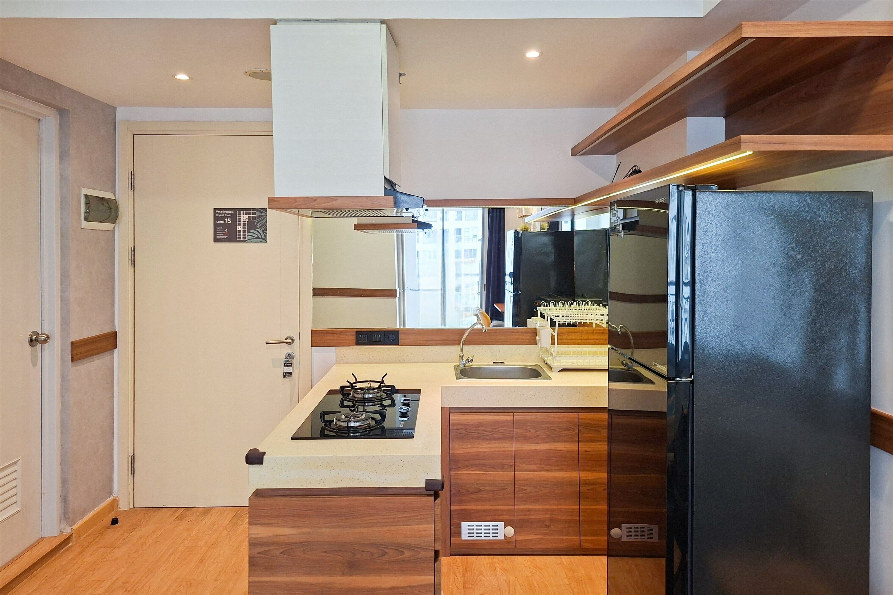 Une cuisine compacte équipée d’une cuisinière à gaz, d’un réfrigérateur noir, de meubles en bois et d’un four encastré.