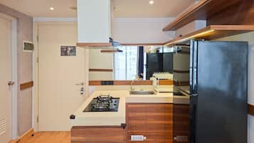 Une cuisine compacte équipée d’une cuisinière à gaz, d’un réfrigérateur noir, de meubles en bois et d’un four encastré.
