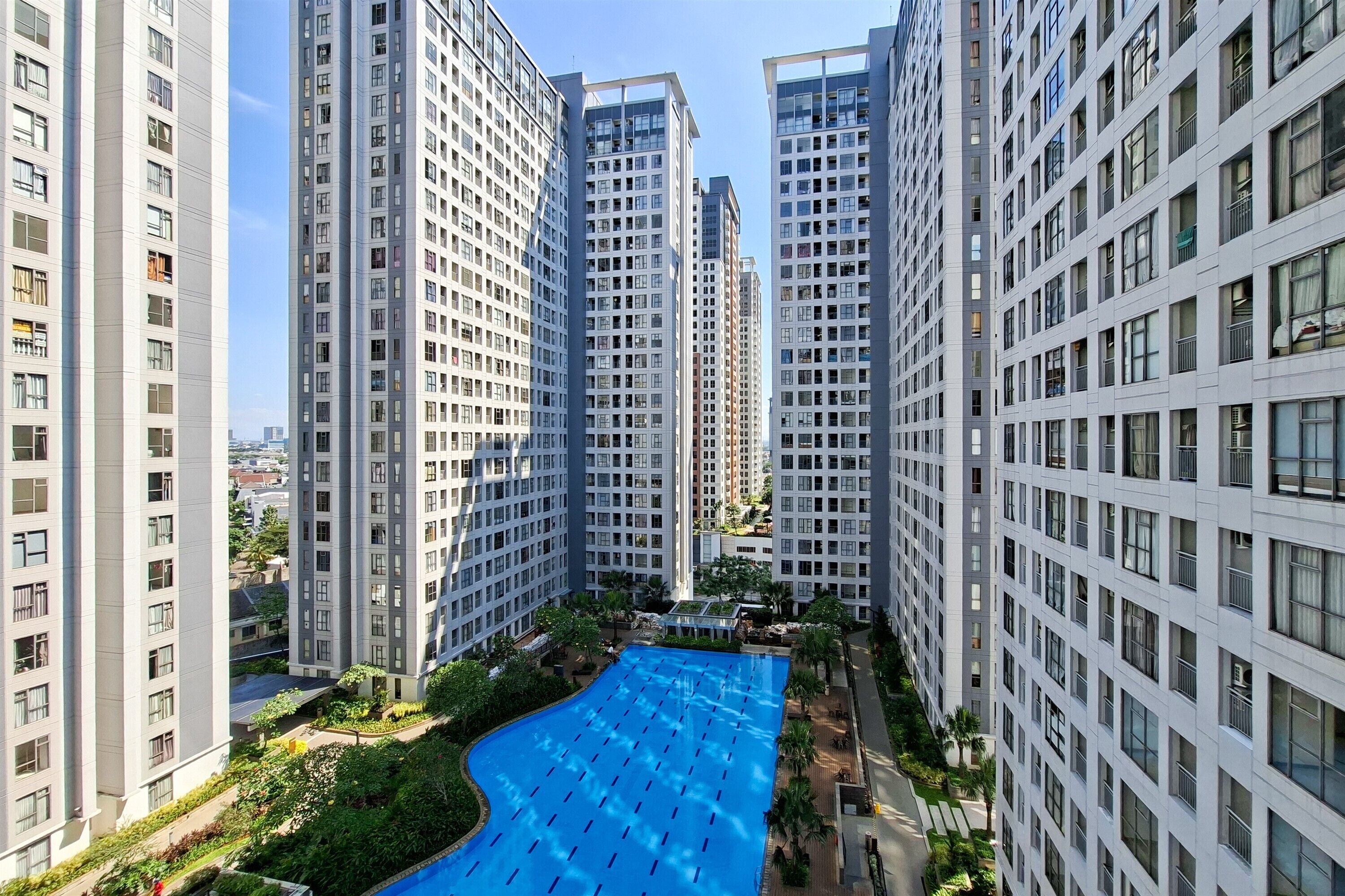 A high-rise residential building with a central swimming pool surrounded by greenery.