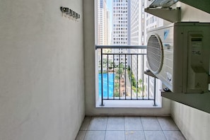 Un balcón estrecho con vistas a una piscina azul y edificios altos.