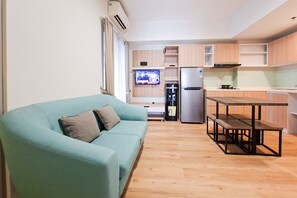 A living room with a sofa, a television, a kitchen with a refrigerator, and a dining table. - Well Appointed 3Br Apartment At M-Town Residence (Tangerang)