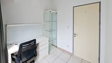 Ein Zimmer mit einem weißen Schreibtisch, einem schwarzen Bürostuhl, einer Glastrennwand und einer geschlossenen Tür.