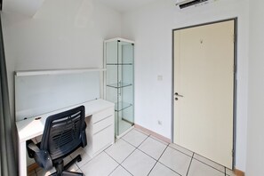 A room with a white desk, black office chair, glass shelving unit, and a closed door. - Warm And Cozy 2Br With Extra Room At Apartment M-Town Residence (Tangerang)