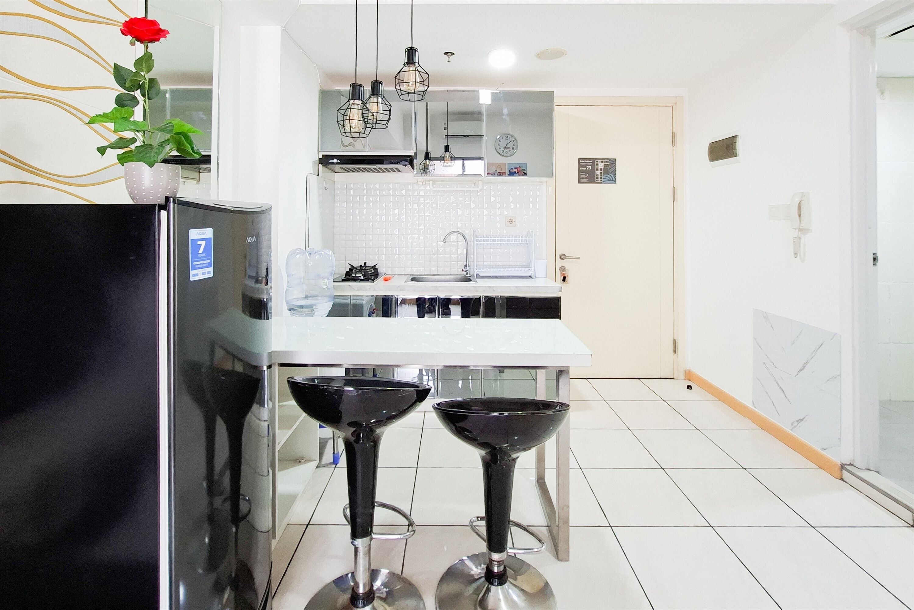 A modern kitchen with a refrigerator, two bar stools, a sink, and a potted plant.