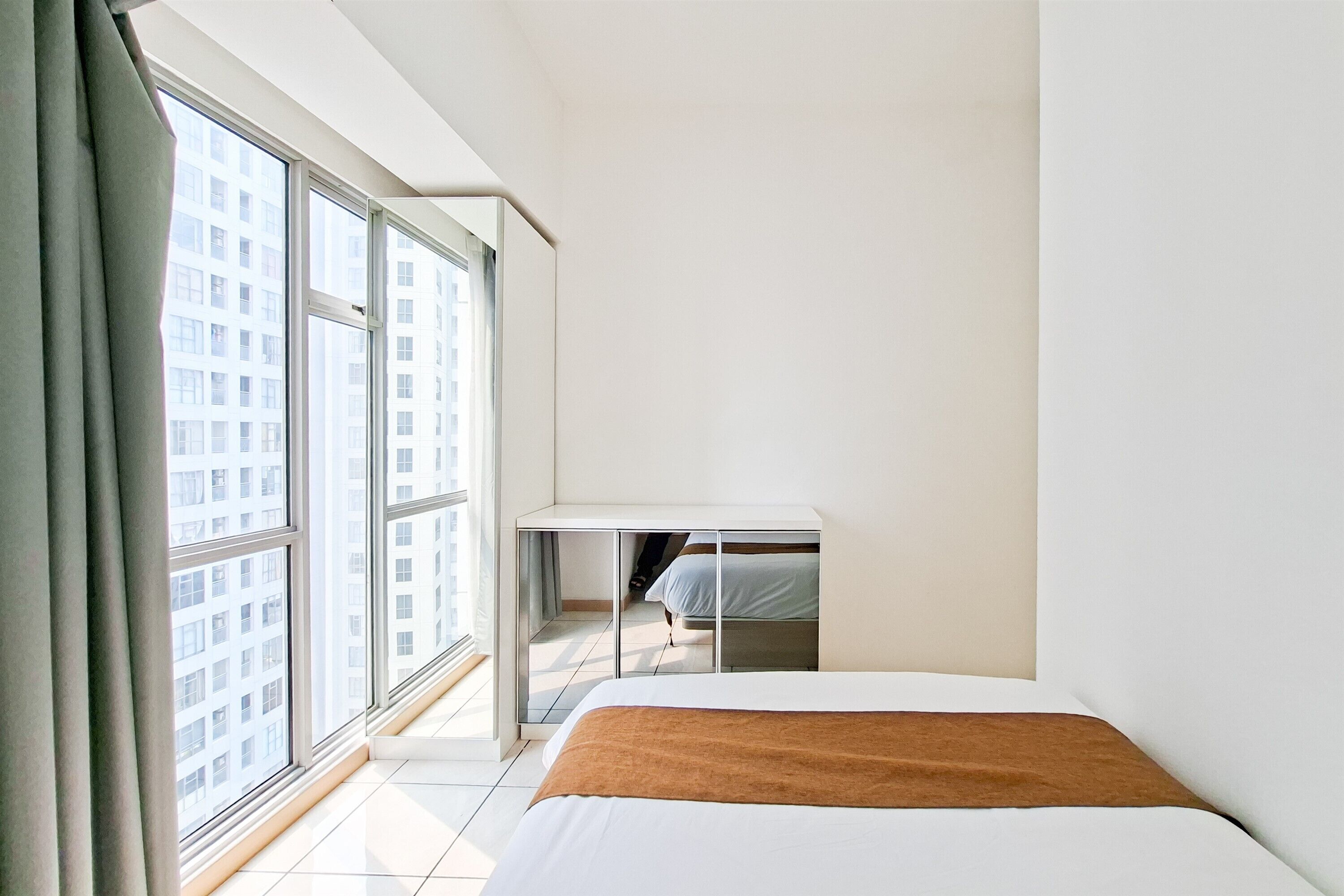 A minimalist hotel room with a large window, a bed, and a small desk.