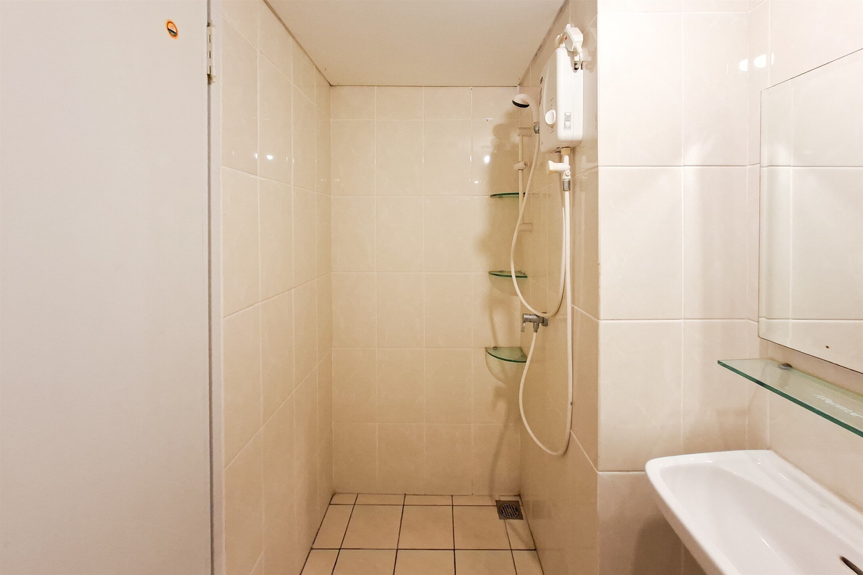 Un pequeño espacio de ducha con azulejos, un estante de vidrio y un lavamanos blanco.