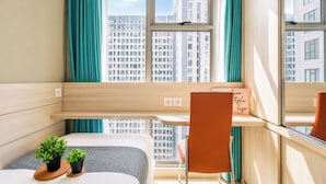 Quarto de hotel moderno com cama, escrivaninha, cadeira e janela com vista para a cidade.