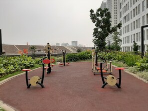 Ein Outdoor-Fitnessbereich mit Trainingsgeräten, umgeben von Grünflächen und einem roten Weg.
