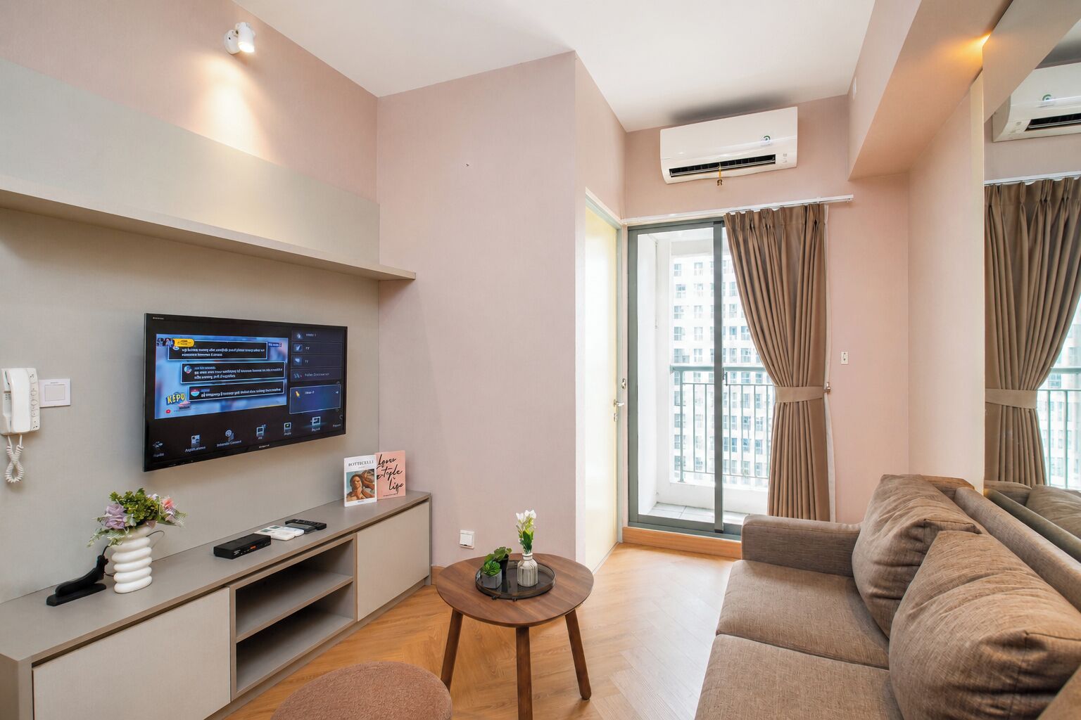 Una sala de estar moderna con un televisor de pantalla plana, un sofá, una mesita y un ventanal con cortinas.