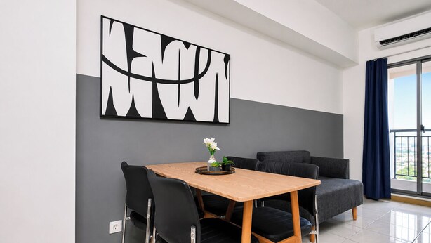 A modern dining area with a wooden table, black chairs, and a grey sofa. - Good Living In Spacious 2Br At Apartment M-Town Residence (Tangerang)