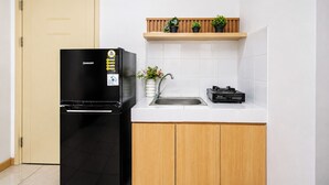 A compact kitchen with a black refrigerator, a sink, a stove, and a wooden shelf with plants. - Good Living In Spacious 2Br At Apartment M-Town Residence (Tangerang)