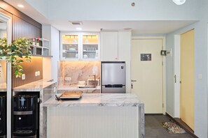A modern kitchen with a marble countertop, built-in cabinets, a stainless steel refrigerator, and a coffee machine. - Cozy Living In Trendy 2Br At Apartment M-Town Residence (Gading Serpong)