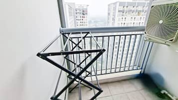 A balcony with a metal drying rack, a window with a view of high-rise buildings, and an air conditioning unit.