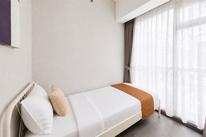 A single bed with white bedding and a brown throw, a window with sheer curtains, and a plain wall. - Cozy Living In Trendy 2Br At Apartment M-Town Residence (Gading Serpong)