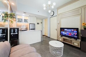 A modern kitchen with built-in appliances, a dining area with a white table and chairs, and a flat-screen TV on a wooden stand. - Cozy Living In Trendy 2Br At Apartment M-Town Residence (Gading Serpong)