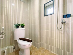 Une salle de bain avec des carreaux à rayures, des toilettes, une douche et un petit miroir.