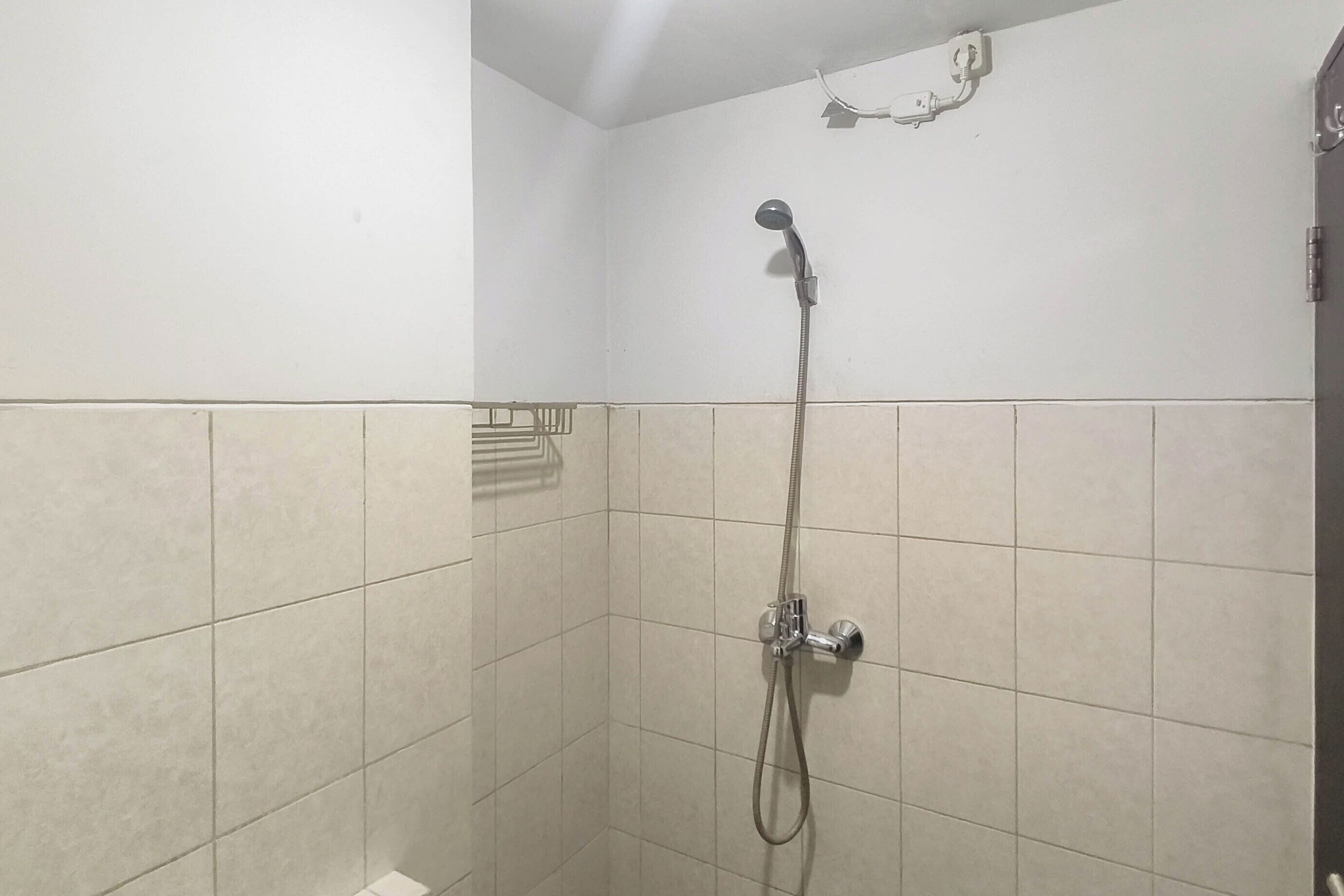 Un pequeño espacio de ducha con azulejos, un cabezal de ducha de mano y un grifo empotrado en la pared.