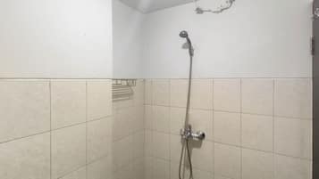 Un pequeño espacio de ducha con azulejos, un cabezal de ducha de mano y un grifo empotrado en la pared.
