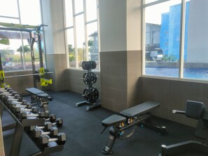 Ein Fitnessstudio mit Krafttrainingsgeräten, einer Bank und großen Fenstern.
