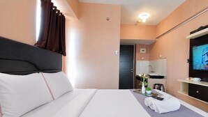 Ein Hotelzimmer mit Bett, Fernseher, einem kleinen Tisch mit Vase und Fernbedienungen sowie einer Badezimmertür.