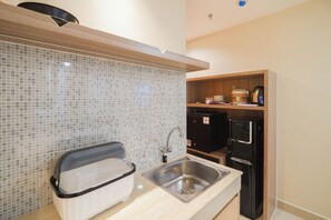 A compact kitchen with a sink, a microwave, a refrigerator, and a tiled backsplash. - Good And Homey Studio At Evenciio Margonda Apartment (Depok)
