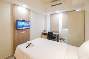 Ein Hotelzimmer mit Bett, Schreibtisch, Stuhl, Wandfernseher und einem fenster mit Vorhängen.