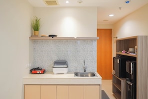 A compact kitchen with a built-in stove, a sink, and a refrigerator. - Good And Homey Studio At Evenciio Margonda Apartment (Depok)