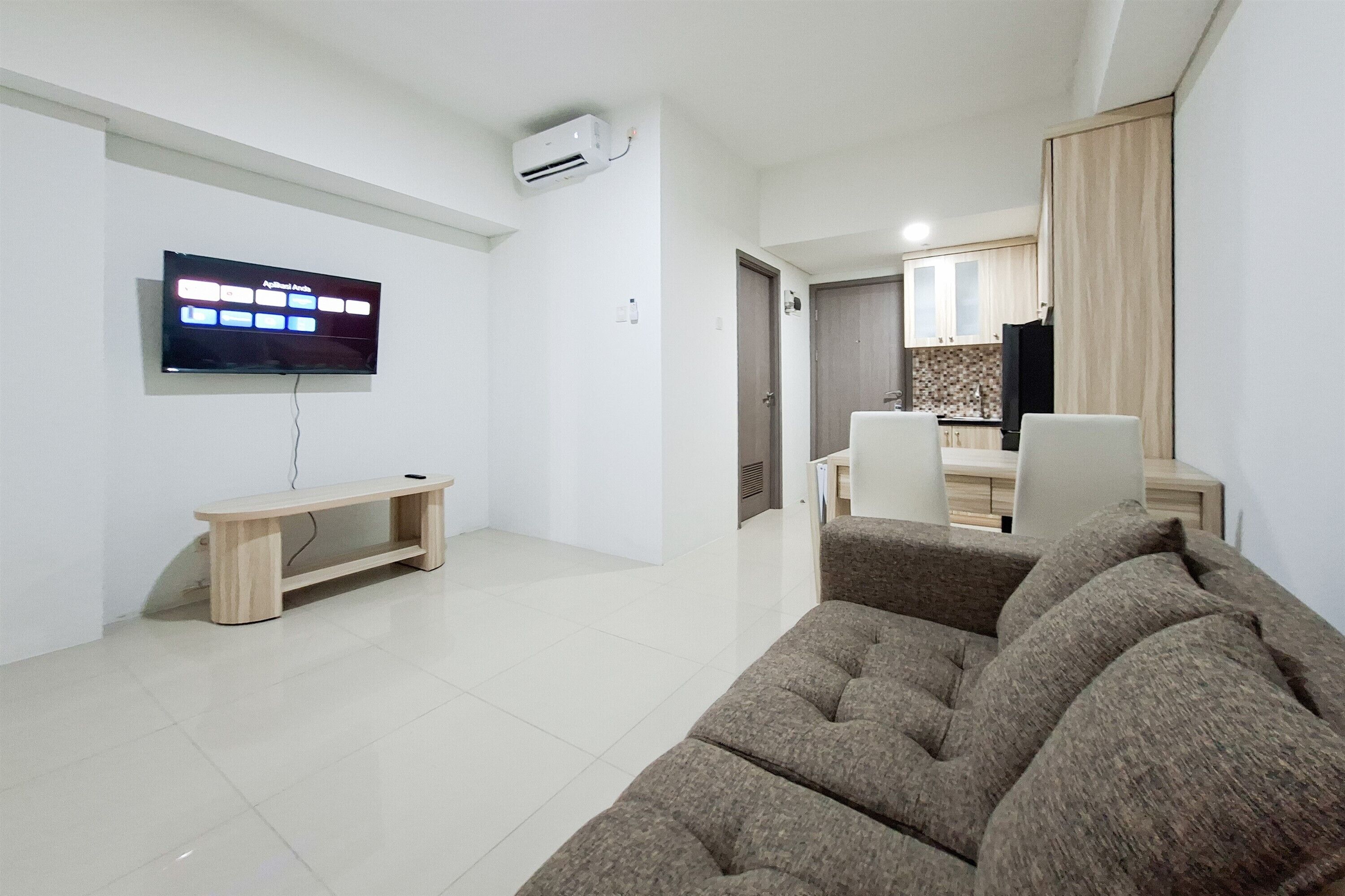 Una sala de estar con televisor, sofá, banca y un área de cocina al fondo.