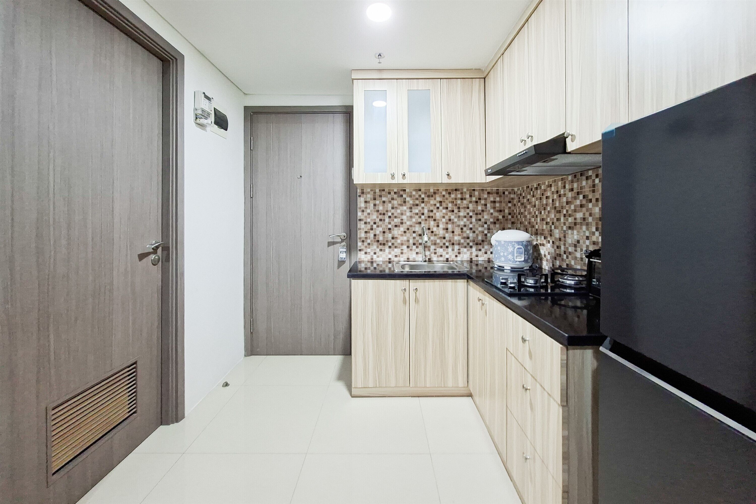Une cuisine compacte avec des meubles en bois, un réfrigérateur noir, un pare-feu en carrelage et une cuisinière à gaz.