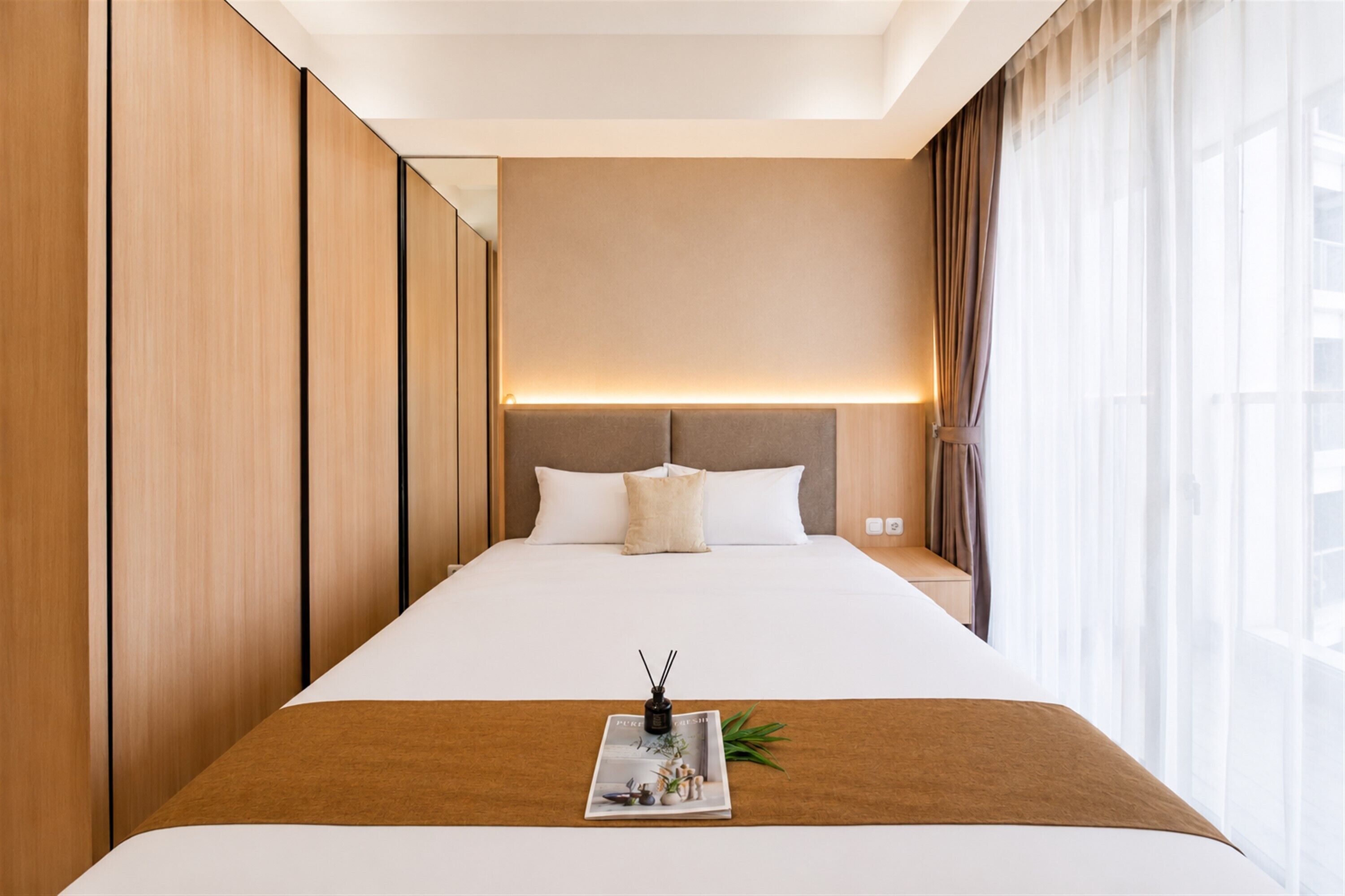 Habitación de hotel con una cama grande, una mesita de noche, cortinas en la ventana y una lámpara de pared.