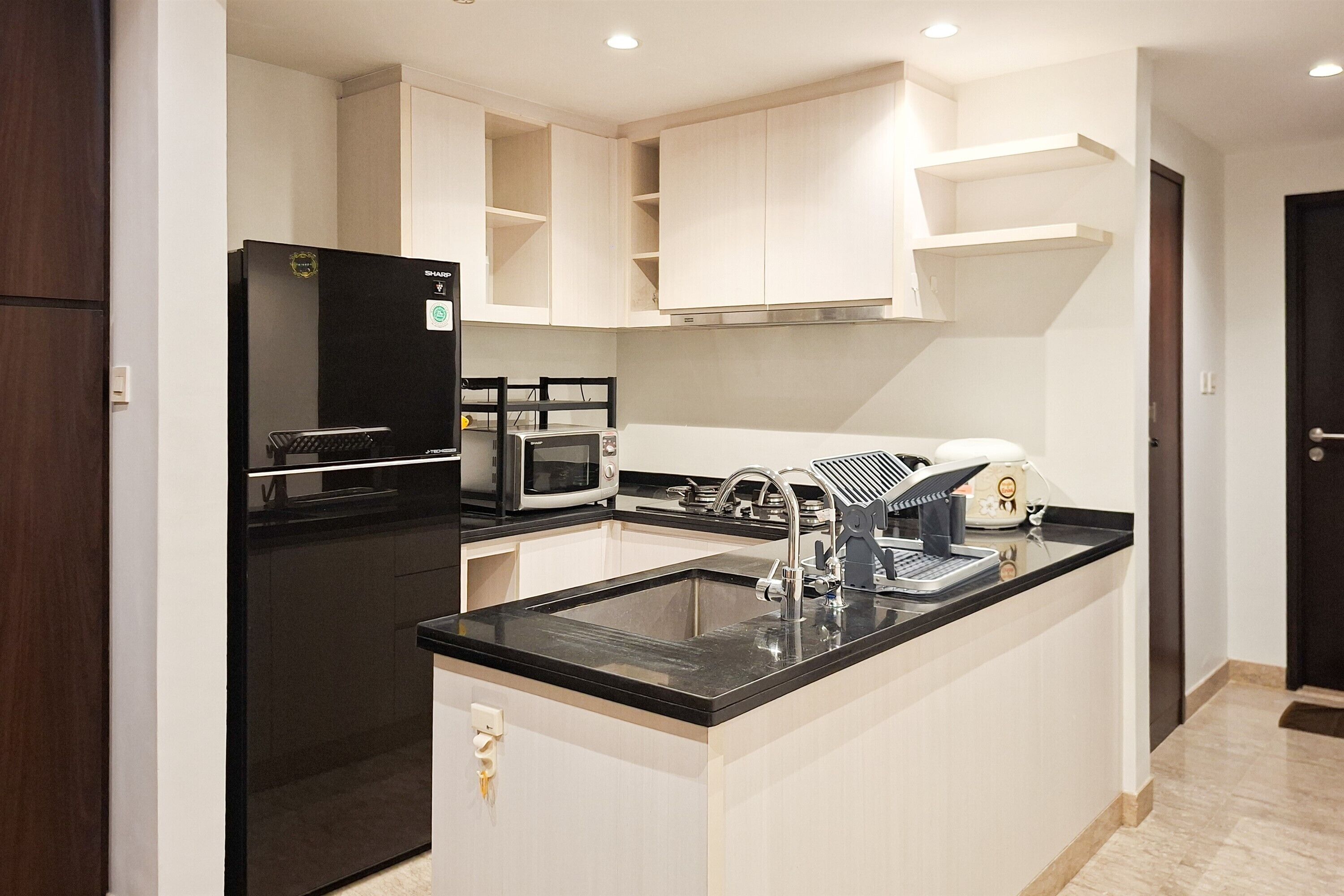 Una cocina moderna con un refrigerador negro, armarios blancos, una encimera negra y un microondas integrado.