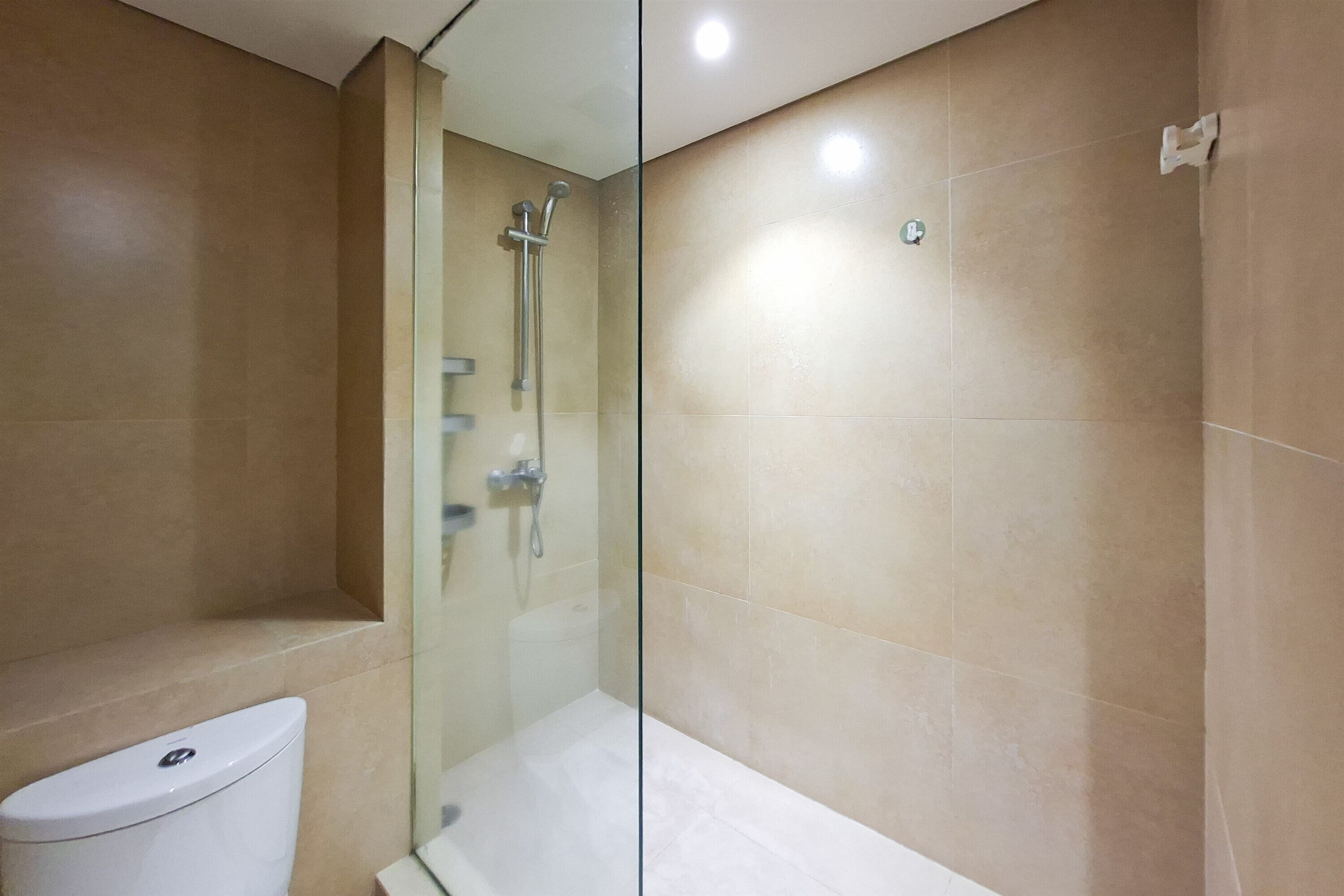 Et badeværelse med en glasvæg omkring bruseniche, toilet og vægge beklædt med beige fliser.
