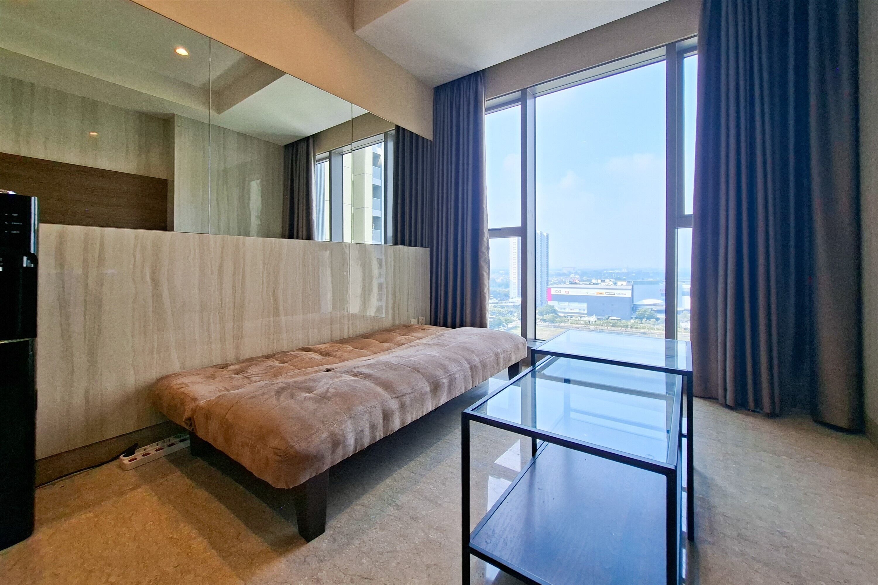 Una habitación de hotel moderna con un ventanal grande, un sofá y una mesa de centro de vidrio.