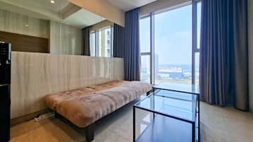 Una habitación de hotel moderna con un ventanal grande, un sofá y una mesa de centro de vidrio.