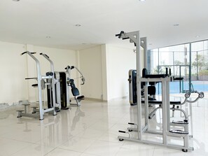A clean, modern gym with various exercise machines, large windows, and a tiled floor. - Best Price And Homey Studio At Pollux Chadstone Apartment (Cikarang)