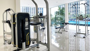 Un gimnasio con varias máquinas de ejercicio, una banca y vistas a una piscina a través de amplios ventanales.