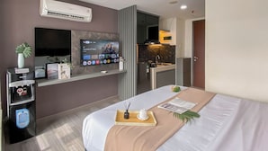 Una habitación de hotel moderna con cama, televisor montado en la pared, minibar y una pequeña kitchenette.