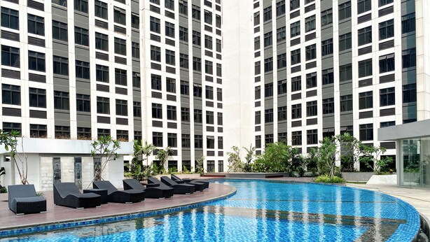 A modern hotel with a large indoor swimming pool surrounded by lounge chairs and greenery. - Compact Studio Near President University At Pollux Chadstone Apartment (Cikarang)